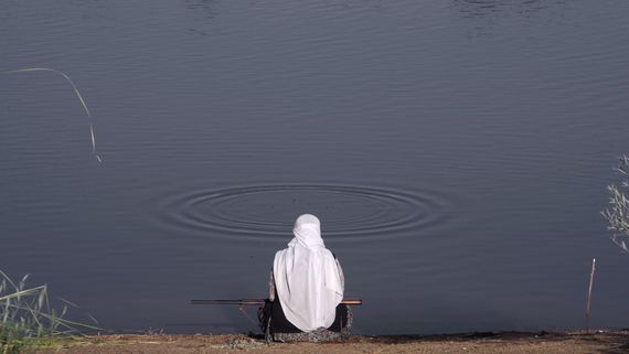 Person in headscarf sitting at lake edge