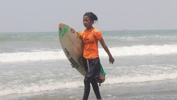 a young woman walking with a surf board under her arm