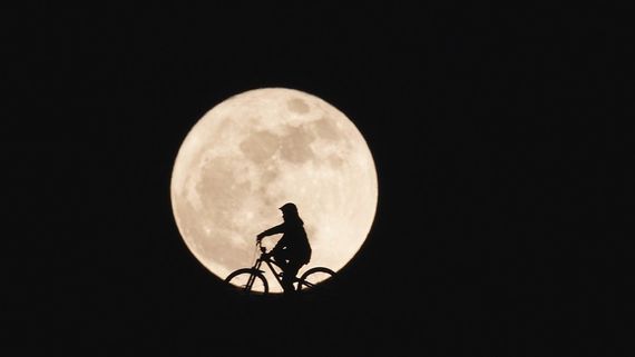 a shadow of someone riding a bike in front of the moon