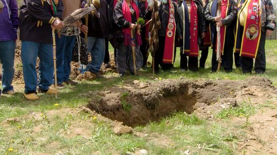 People in Indigenous dress around open grave