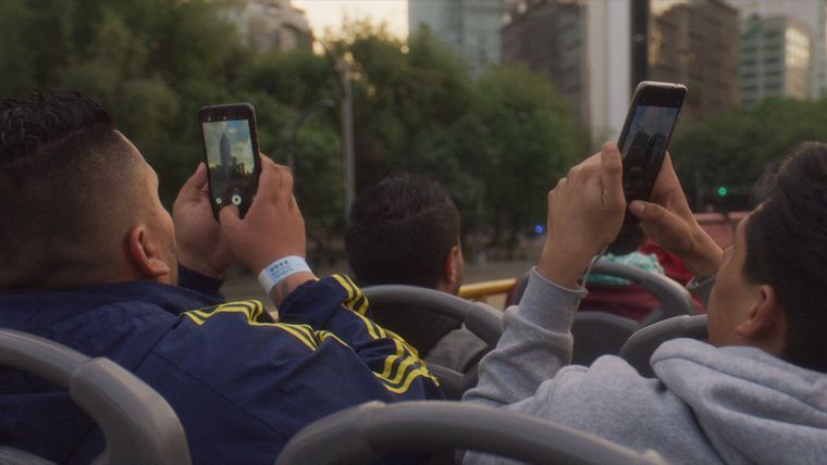 people on the top level of an open bus taking photos of the buildings above them