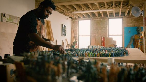 a man working in a studio with a table full of little army figurines