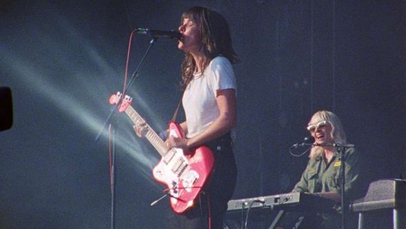 a woman playing guitar and singing with another woman playing keyboard