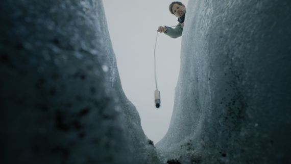 someone leaning over a glacier holding a microphone into it