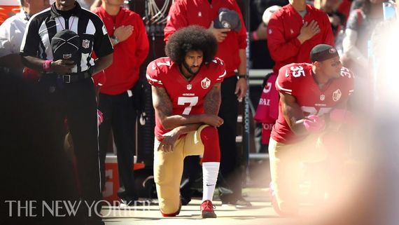 football players taking a knee while others stand behind them