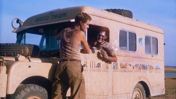 a man leaning on a bus while speaking to another man in the driver's seat