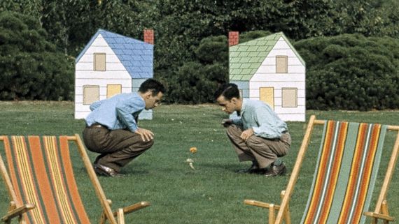 two men crouched down in front of two houses