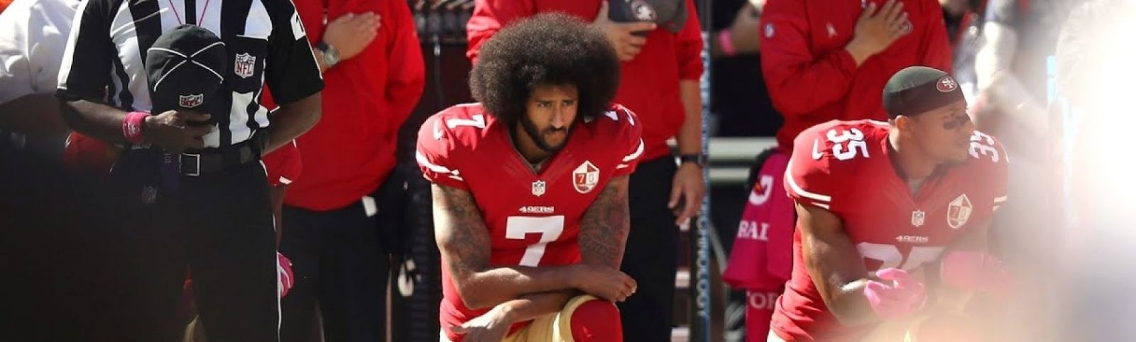 football players taking a knee while others stand behind them