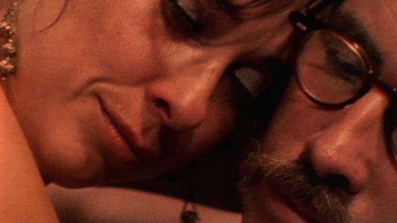 closeup of a woman with earrings and a man with facial hair and glasses pressing their faces together