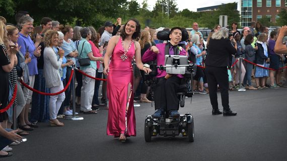 a couple in black tie, one in a wheelchair, walking a roped off area